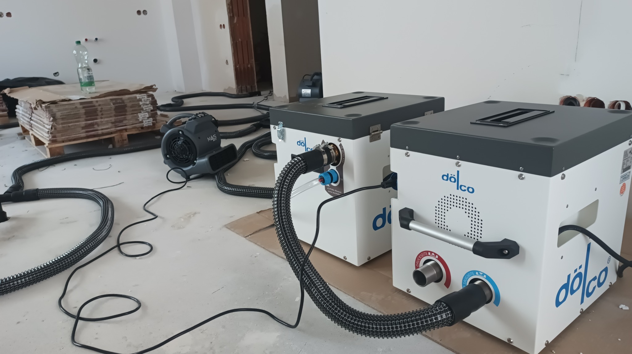 Osuszanie posadzki w Rudzie Śląskiej. Dwa osuszacze kondensacyjne Dölco, wentylator MAS 811 i rury na surowej posadzce w trakcie pracy.