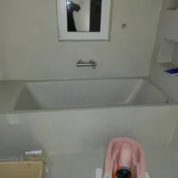 Nowoczesna, zabudowana wanna w łazience wykończonej w jasnych odcieniach szarości, z minimalistyczną armaturą i wbudowaną półką, widoczne akcesoria do montażu wanny.