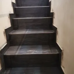 Schody wyłożone ciemną, grafitową glazurą imitującą drewno, z widocznymi śladami prac glazurniczych na ścianach i fugach.