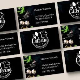 Zestaw czarnych wizytówek z białym logo firmy cateringowej, zawierającym motyw nakrycia i czapki kucharskiej, oraz dane kontaktowe.