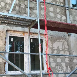 Montaż okien w budynku z elewacją w trakcie prac, widoczne rusztowanie i czerwona lina.