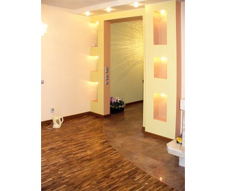 Wnętrze domu po remoncie: parkiet ułożony w łuk, żółte ściany z wnękami oświetlonymi punktowo, widoczne kwiaty w doniczce i czajnik elektryczny.