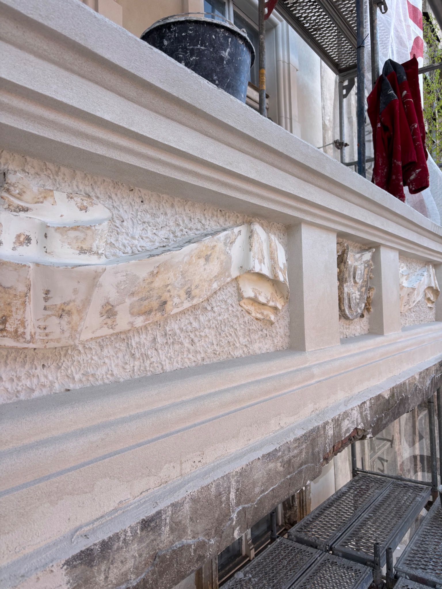 Fragment odnowionej balustrady z dekoracyjnymi elementami na tle rusztowania i elewacji budynku. Widoczne ślady prac renowacyjnych.