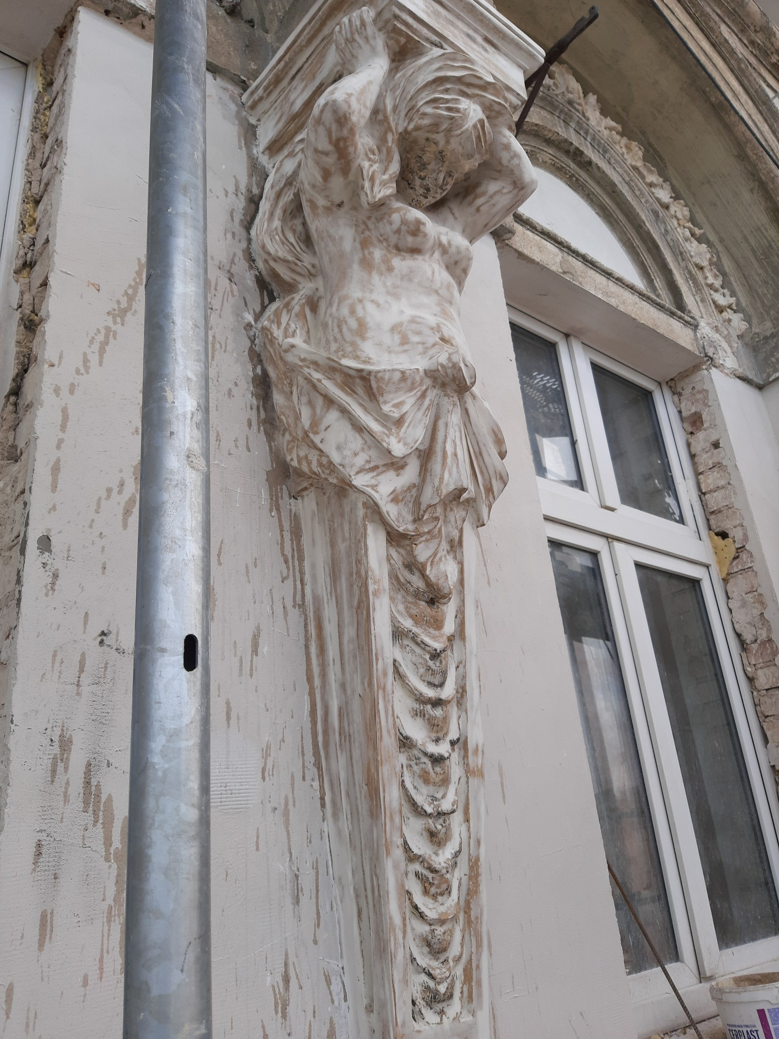 Renowacja elewacji kamienicy: figura kobiety podtrzymująca okno, widoczne ślady prac konserwatorskich i rusztowanie.