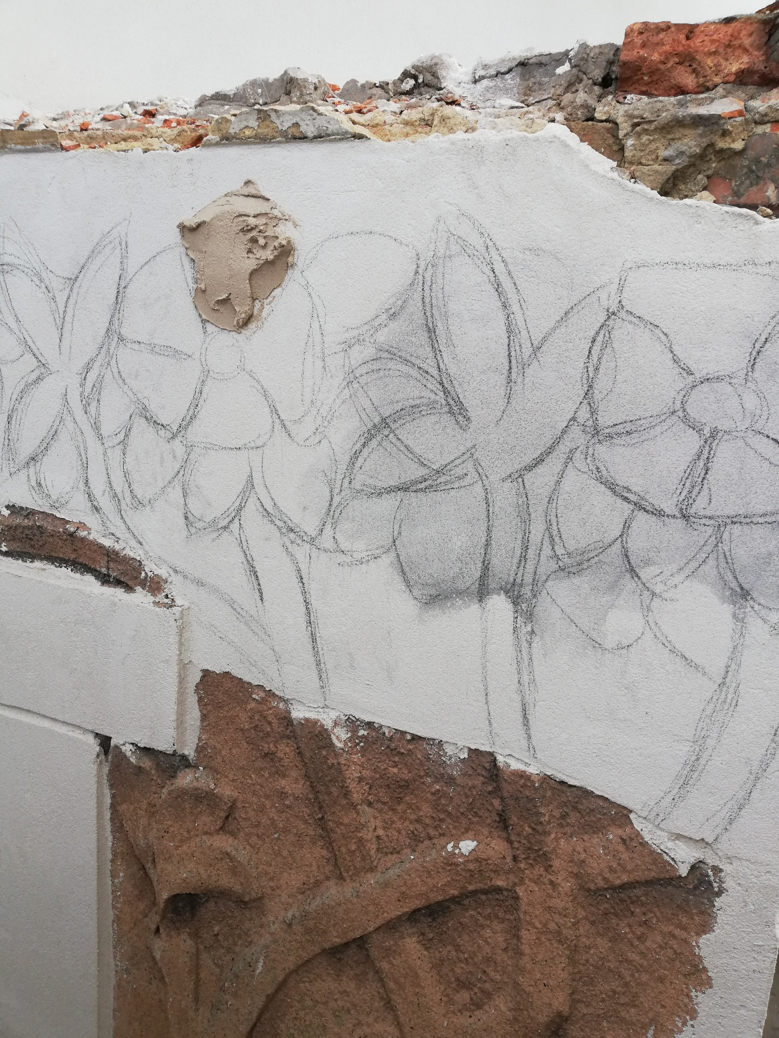 Ściana z uszkodzonym tynkiem i szkicem kwiatów w Poznaniu, fragment dekoracyjnego elementu architektonicznego z piaskowca u dołu.