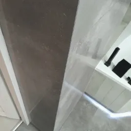 Wykończony narożnik łazienki z ciemnoszarą płytką imitującą kamień, widoczna kabina prysznicowa z czarną armaturą i podświetleniem LED przy podłodze.