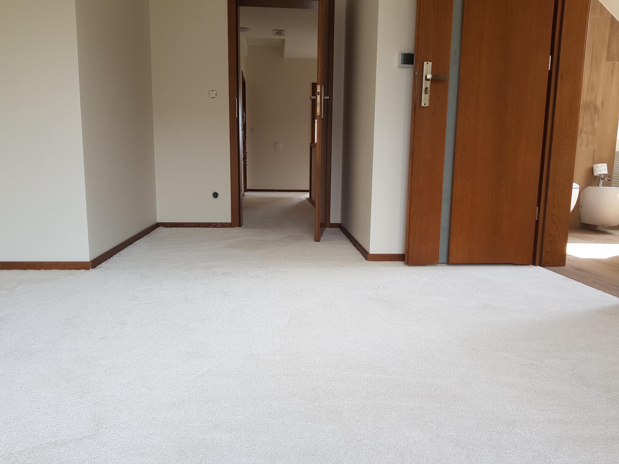 Jasny, puszysty dywan w pokoju z otwartymi drzwiami i widoczną łazienką w tle.