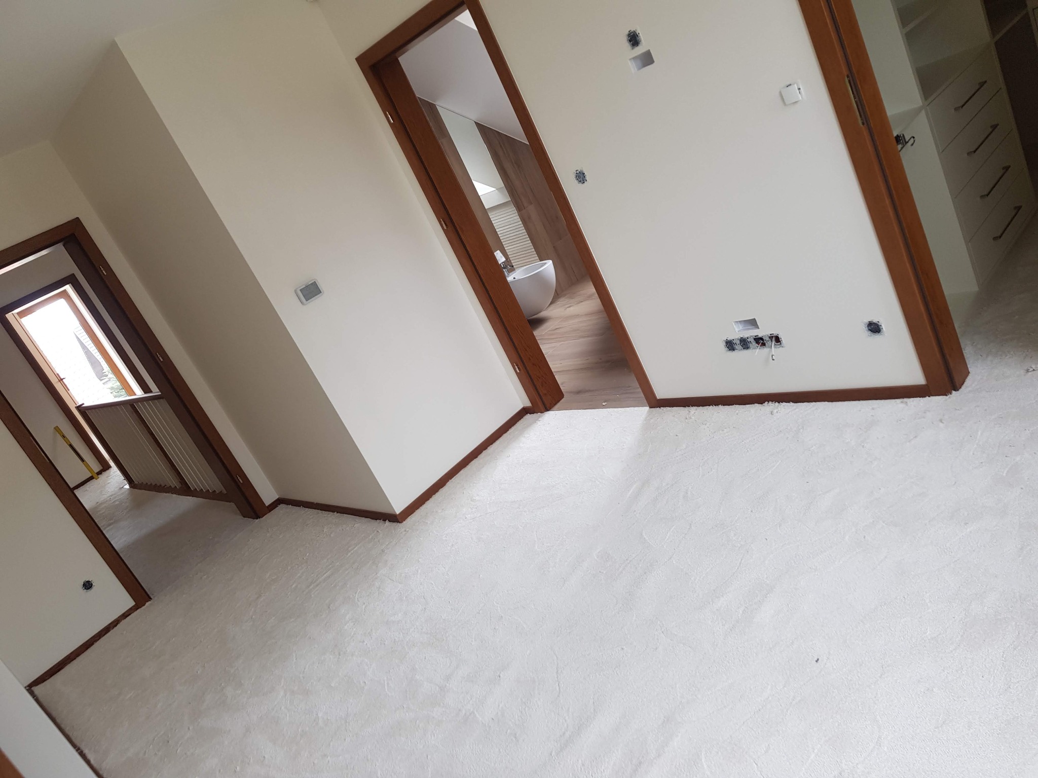 Przygotowanie podłoża pod panele lub parkiet: wylewka samopoziomująca, widoczne drzwi z brązowymi ościeżnicami, ściany w kolorze złamanej bieli, instalacje elektryczne w puszkach.