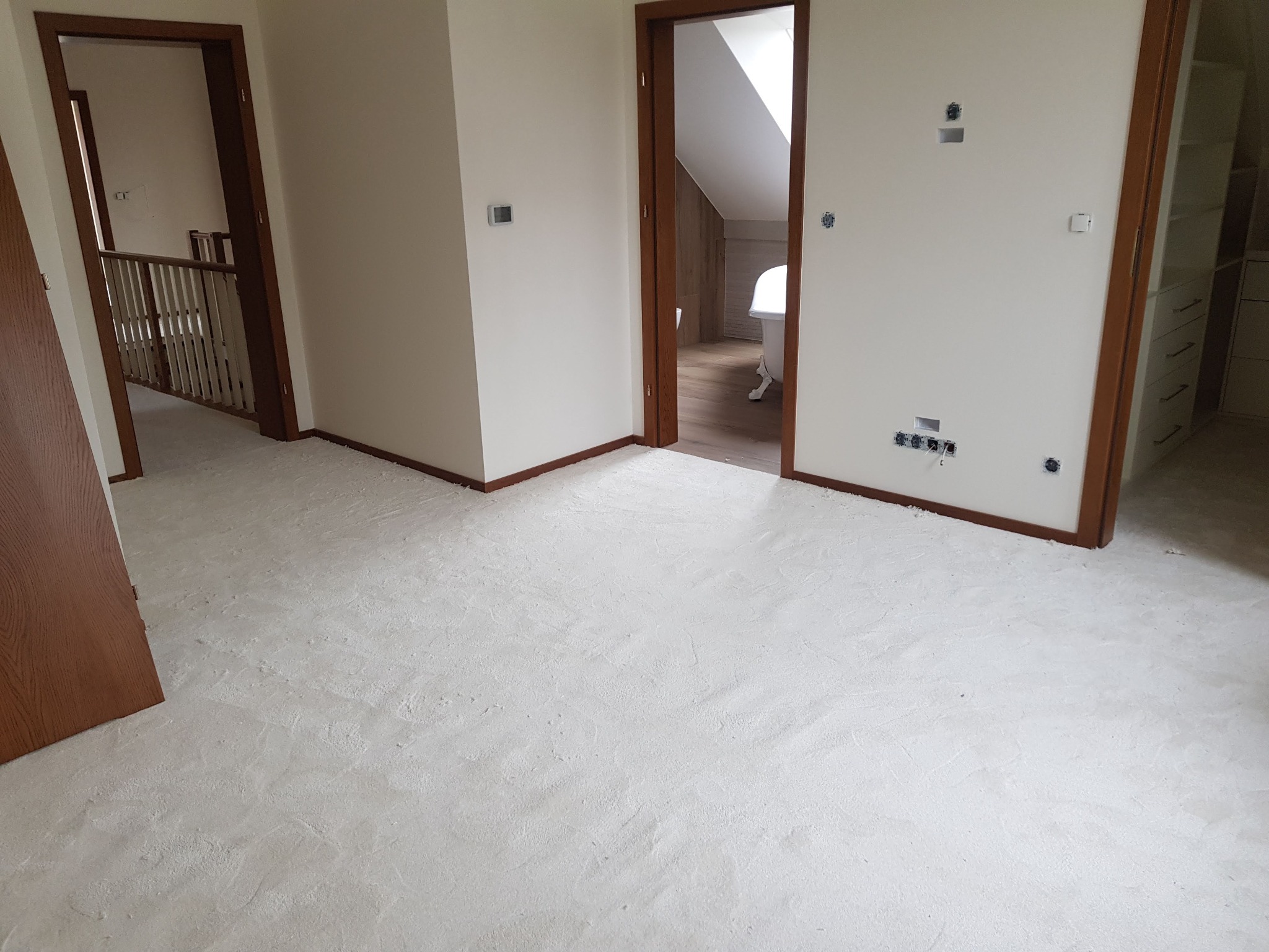 Przygotowane podłoże pod montaż paneli lub parkietu, widoczne wylewki wyrównujące poziom w pomieszczeniu z trzema otworami drzwiowymi.