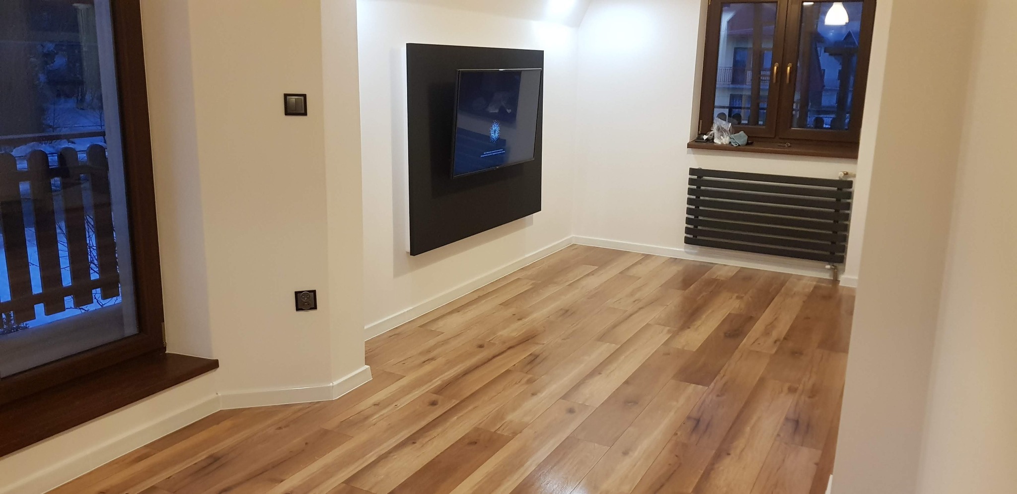 Jasne panele podłogowe w nowocześnie urządzonym pokoju z telewizorem na ścianie i grzejnikiem pod oknem.