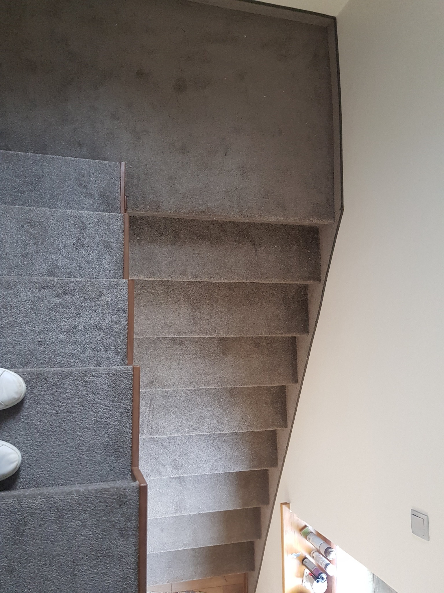 Szare schody obite wykładziną dywanową z brązowymi listwami, widok z góry z fragmentem buta