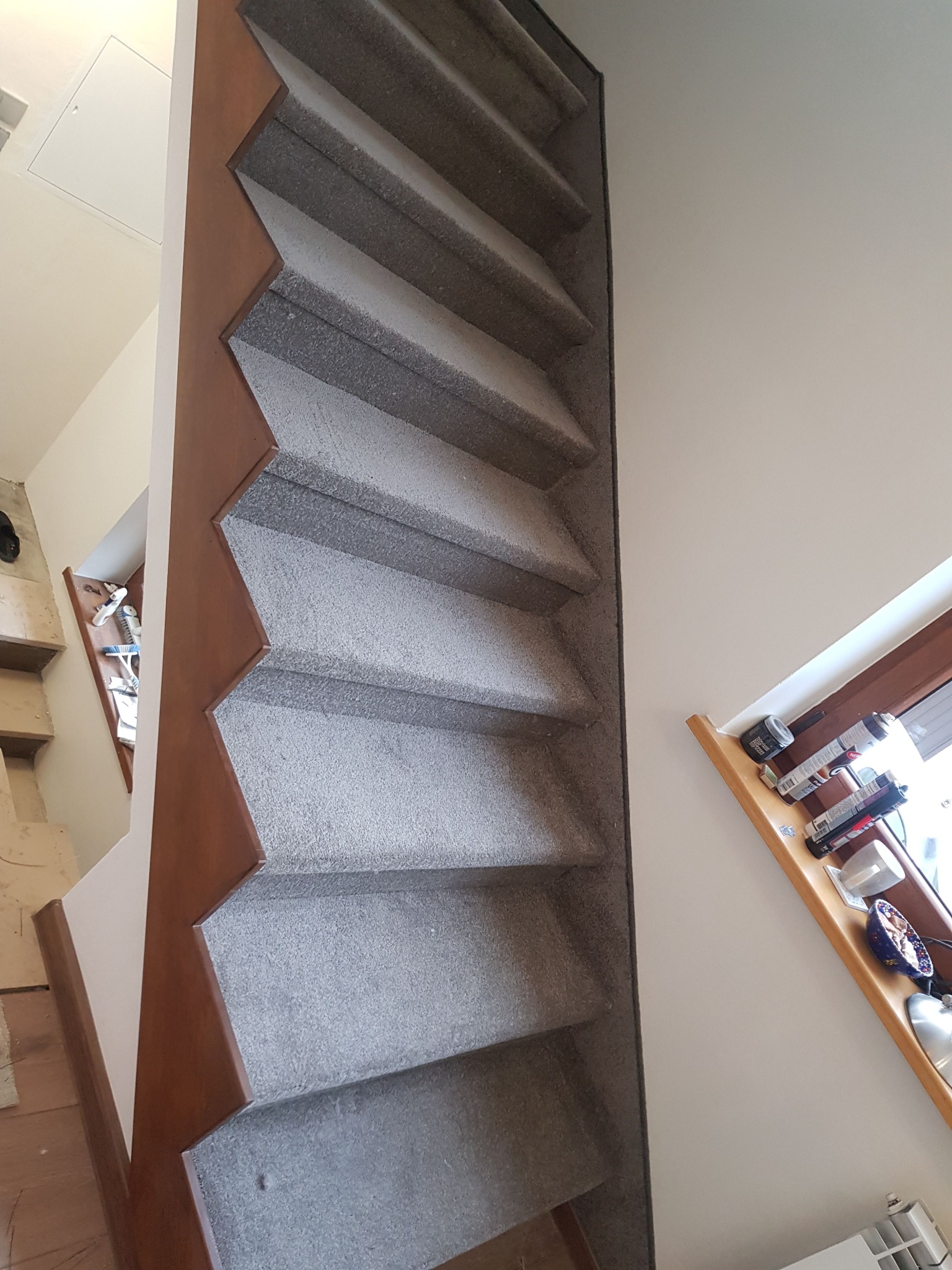Schody z szarą wykładziną dywanową, brązowe wykończenie, widok z góry, półka okienna z akcesoriami malarskimi.