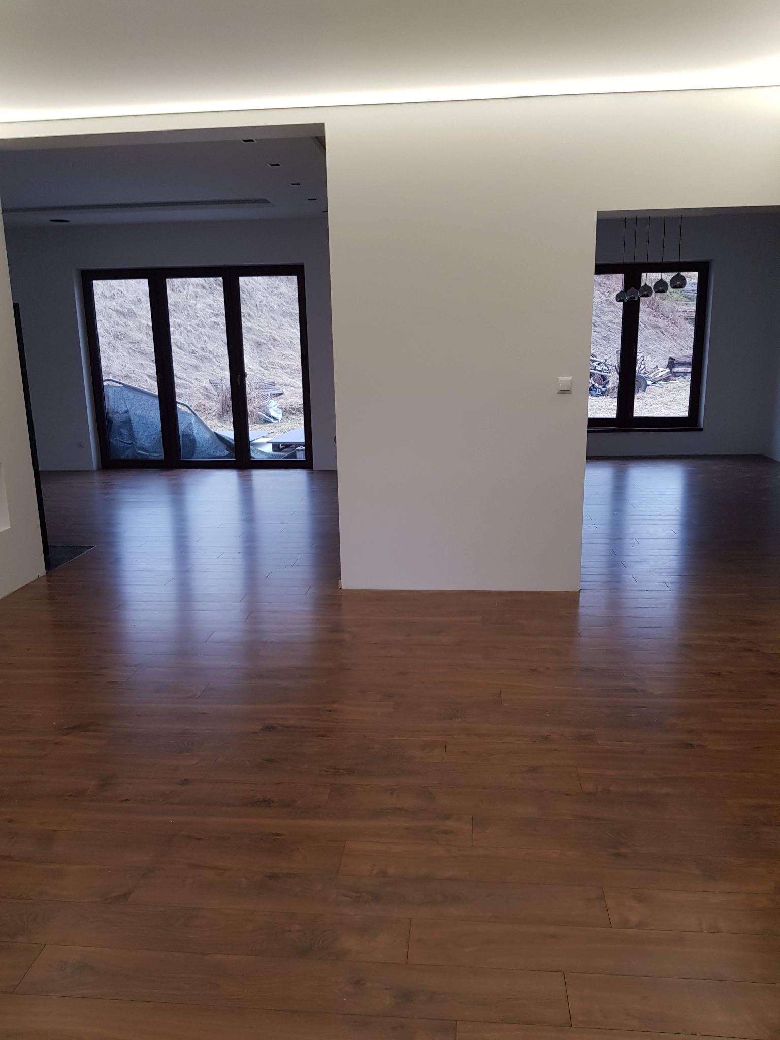 Nowo ułożona, błyszcząca podłoga z paneli w odcieniach brązu, widok na dwa puste pokoje z oknami wychodzącymi na zewnątrz.