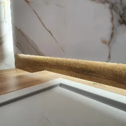 Fragment łazienki z marmurową ścianą, drewnopodobną zabudową i podświetleniem LED, ukazujący szczegóły wykończenia.