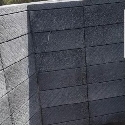 Usługi remontowe - Fragment nowej, grafitowej elewacji z bloczków betonowych w Toruniu, z widocznym narożnikiem i fragmentem podłoża z jasnych płyt.