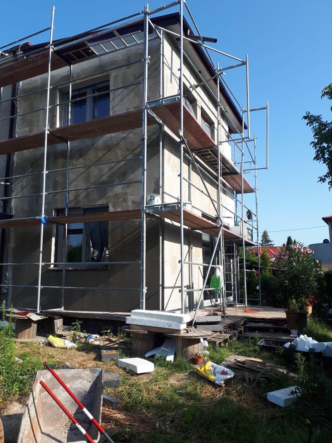 Dom w trakcie ocieplania elewacji, widoczne rusztowania, styropian i wiadro z farbą na podeście.