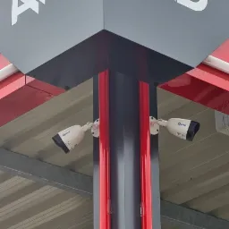 Dwie kamery przemysłowe marki OMAZI zamontowane na słupie z logo AWD, widoczne elementy konstrukcji dachu.