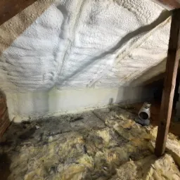 Poddasze z ociepleniem pianką PUR na skośnym dachu, widoczna ceglana ściana, fragment drewnianej konstrukcji oraz stara wełna mineralna na podłodze, oraz nagrzewnica.