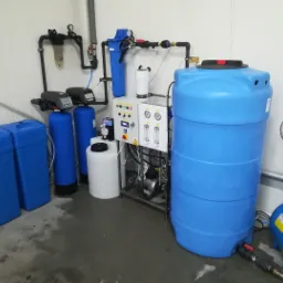 Kompletna instalacja uzdatniania wody w pomieszczeniu technicznym, widoczne filtry, zbiorniki, pompy i panel sterowania, z elementami w kolorze niebieskim i białym.