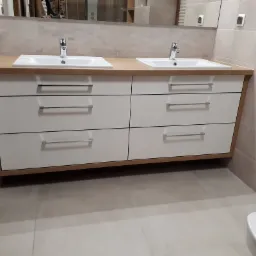 Łazienka z dwiema umywalkami nablatowymi na szafce z białymi frontami szuflad i drewnianym blatem, widok z perspektywy podłogi.