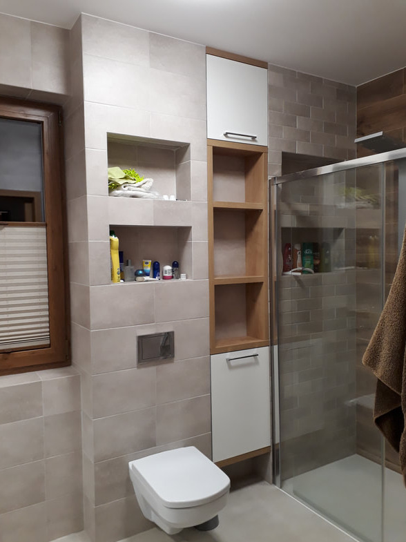 Nowoczesna łazienka z zabudową z drewnianymi akcentami, wisząca toaleta, kabina prysznicowa i półki wnękowe z kosmetykami i ręcznikami.