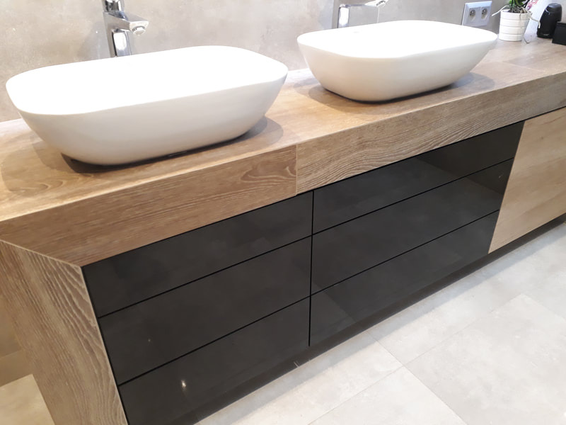 Łazienka z dwiema owalnymi umywalkami nablatowymi na drewnianym blacie z szafkami z czarnymi, lakierowanymi frontami szuflad.