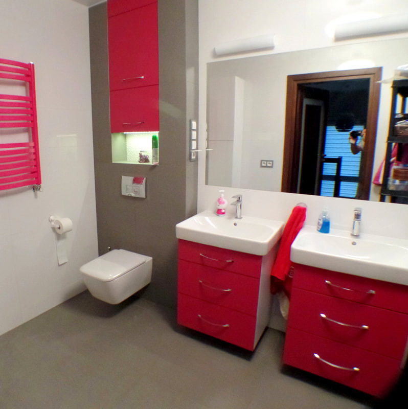 Nowoczesna łazienka z dwoma umywalkami na szafkach w odcieniach różu, wisząca toaleta i grzejnik drabinkowy w kolorze fuksji, odbicie fotografa w lustrze.