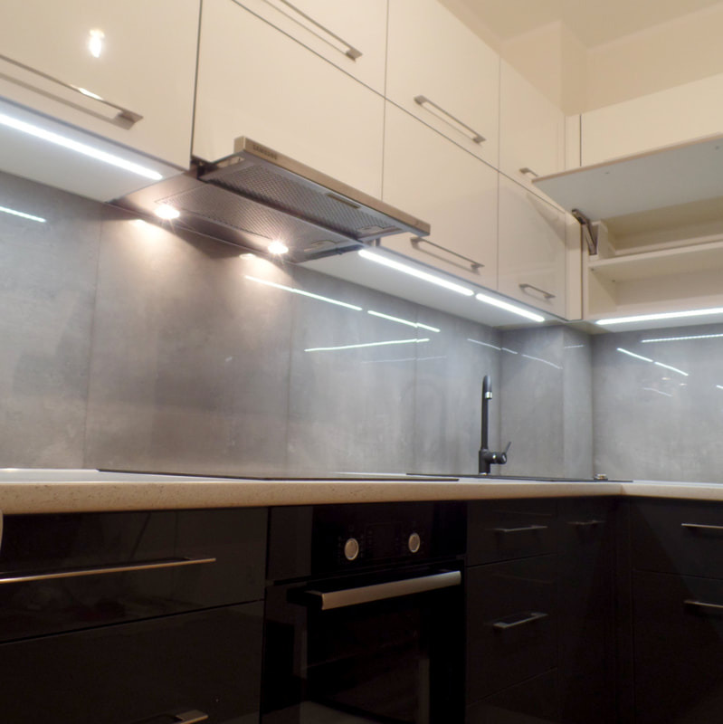 Nowoczesna kuchnia z czarnymi błyszczącymi szafkami dolnymi, jasnymi szafkami górnymi, szarym panelem nad blatem, oświetleniem LED pod szafkami i czarną armaturą.