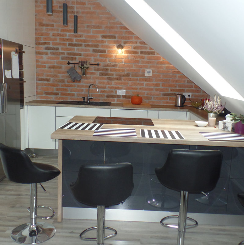 Nowoczesna kuchnia na poddaszu z ceglaną ścianą, blatem z motywem zebry, czarnymi hokerami i halogenowym oświetleniem.