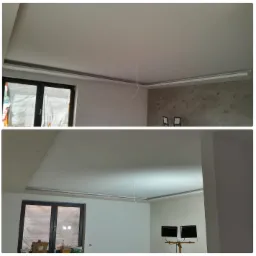 Wykończone wnętrze z gładzią na suficie i ścianach, widoczne listwy dekoracyjne pod sufitem, okno i fragment ściany z dekoracyjnym tynkiem.