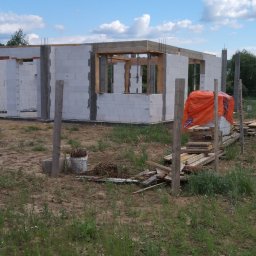 Eugeniusz Dobrovolskyi - Wznoszona konstrukcja domu z betonu komórkowego, widoczne drewniane nadproża i zbrojenia, na pierwszym planie składowane materiały budowlane przykryte pomarańczową folią.