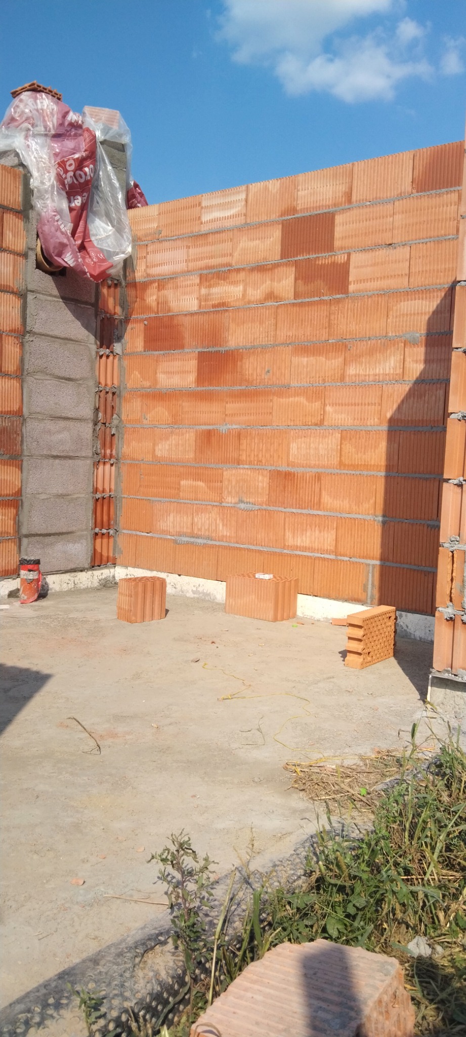 Wznoszenie ścian z ceramicznych pustaków, widoczne poziome spoiny wzmacniające, częściowo przykryte folią ochronną, na fundamencie z betonu komórkowego.