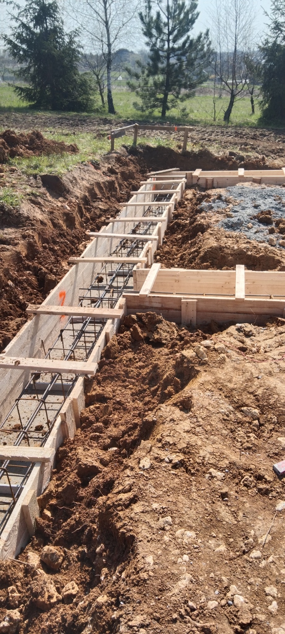 Szalunek zbrojony stalą przygotowany do wylania betonu pod fundament domu, widok z góry na wykopaną ziemię i drewniane elementy konstrukcji.