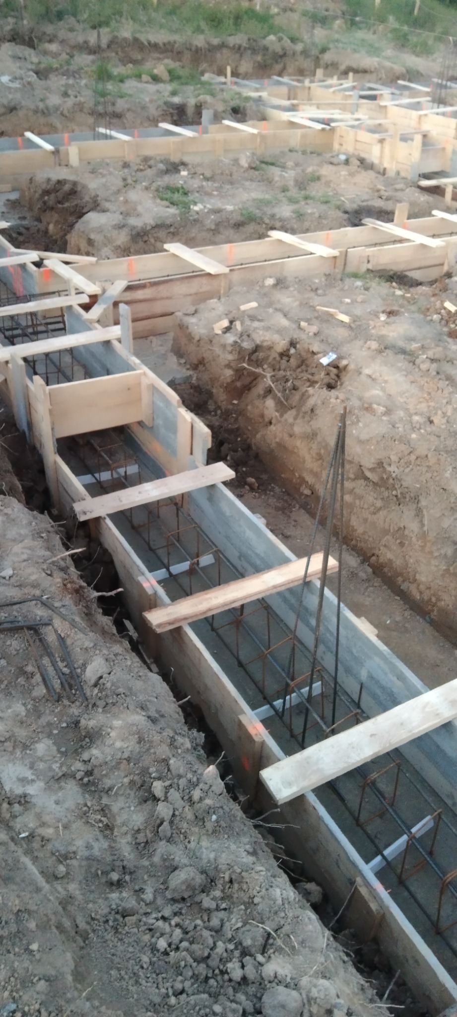 Szalunki zbrojeniowe przygotowane do zalania betonem w wykopie pod fundamenty, widoczne drewniane elementy konstrukcyjne i stalowe pręty zbrojeniowe.