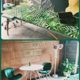 Wnętrze gabinetu z leżanką pokrytą tkaniną w tropikalne liście, stolikiem z dwoma zielonymi krzesłami i lampą grzewczą, utrzymane w zielono-naturalnej tonacji.