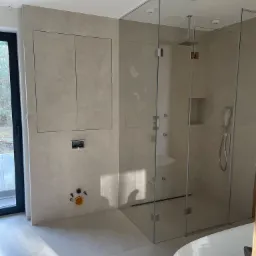 Nowoczesna łazienka z kabiną prysznicową typu walk-in, wykończona płytkami w odcieniach beżu, z ukrytą szafką i minimalistyczną armaturą.