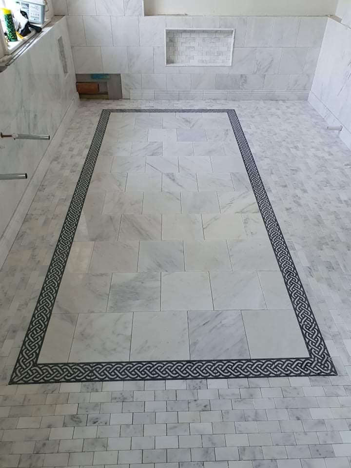 Wykończona łazienka z marmurową podłogą i ścianami, dekoracyjna bordiura z motywem plecionki, wnęka w ścianie wyłożona mozaiką.