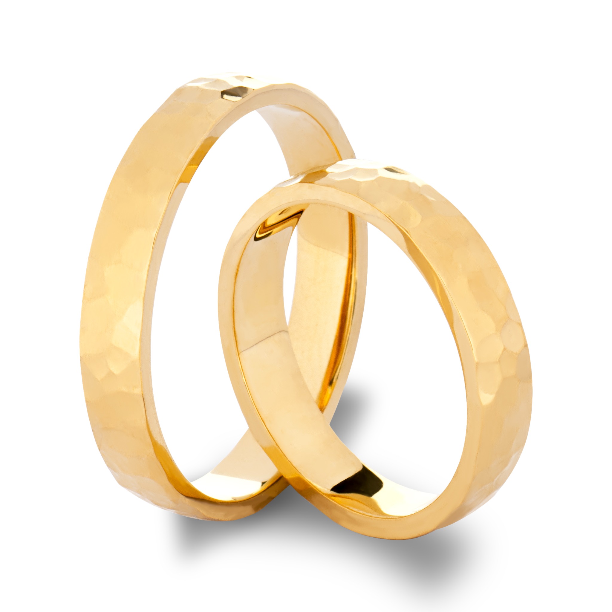 Dwa złote obrączki ślubne z młotkowaną fakturą, leżące na białym tle z delikatnym cieniem.