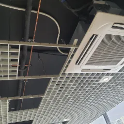 Kasetonowa klimatyzacja sufitowa marki Tadiran, widoczna instalacja rur i przewodów na czarnym suficie podwieszanym z kratownicą.