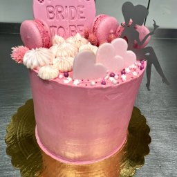 CATERING TRADYCJA PATRYCJA JASIŃSKA - Różowy tort na złotym podkładzie, udekorowany makaronikami, bezami, różowymi sercami i topperem z napisem 'Kaja Bride to be' oraz sylwetką kobiety.