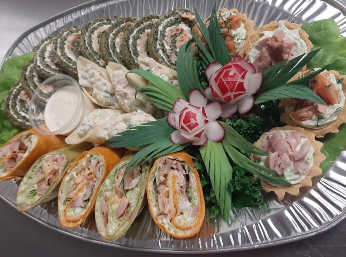 Elegancka srebrna taca z różnorodnymi przekąskami: roladki szpinakowe, muszle makaronowe z farszem, tortille z nadzieniem i mini tartaletki z kremem i łososiem, udekorowane rzodkiewkami w kształcie...
