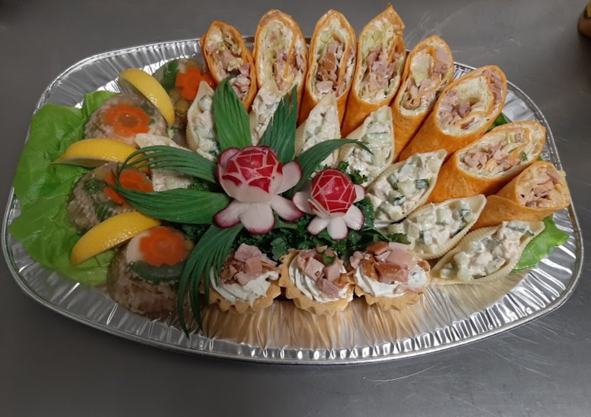 Srebrna patera z galaretkami, roladkami, muszelkami z sałatką i tartaletkami, dekorowana rzodkiewkowymi różyczkami i zielonymi liśćmi.