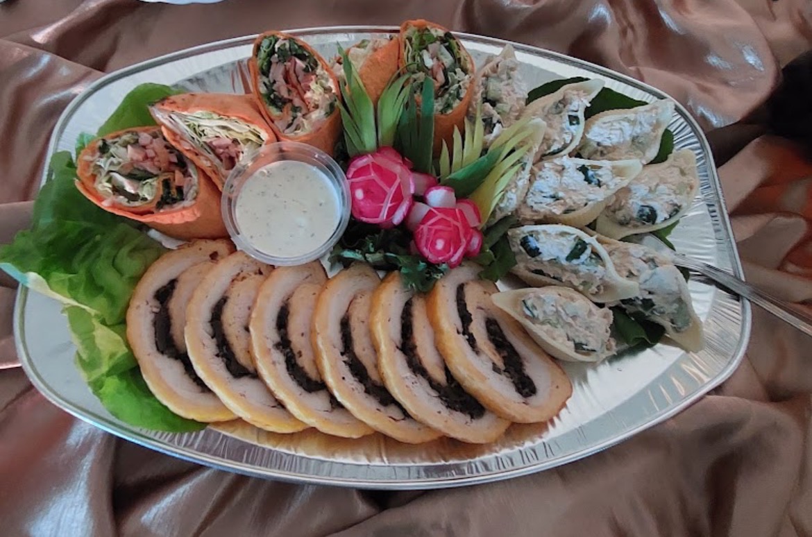 Dekoracyjna srebrna patera z roladkami z tortilli, roladą z kurczaka z farszem, muszelkami makaronowymi z farszem, dipem i dekoracjami z warzyw.