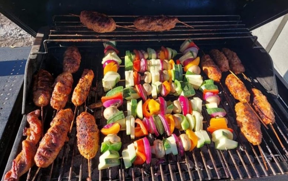 Szpadki z warzywami (papryka, cukinia, cebula, pieczarki) i mięsne szaszłyki na grillu, przygotowywane na świeżym powietrzu.