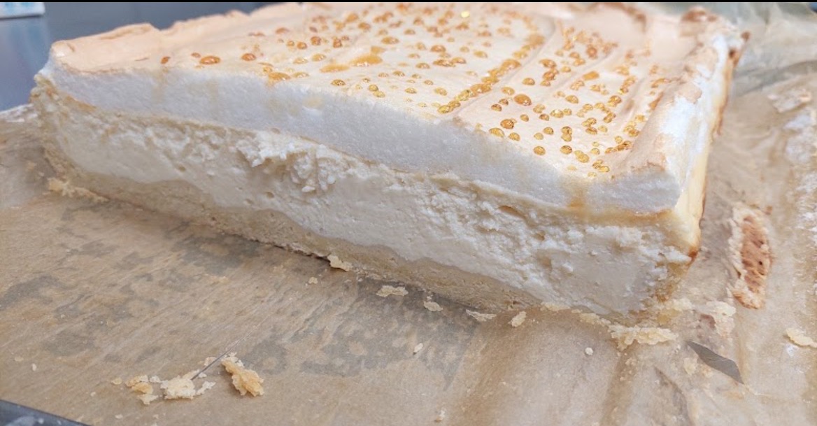 Kawałek sernika z bezą i karmelizowanymi kropelkami, leżący na papierze do pieczenia, z bliska.