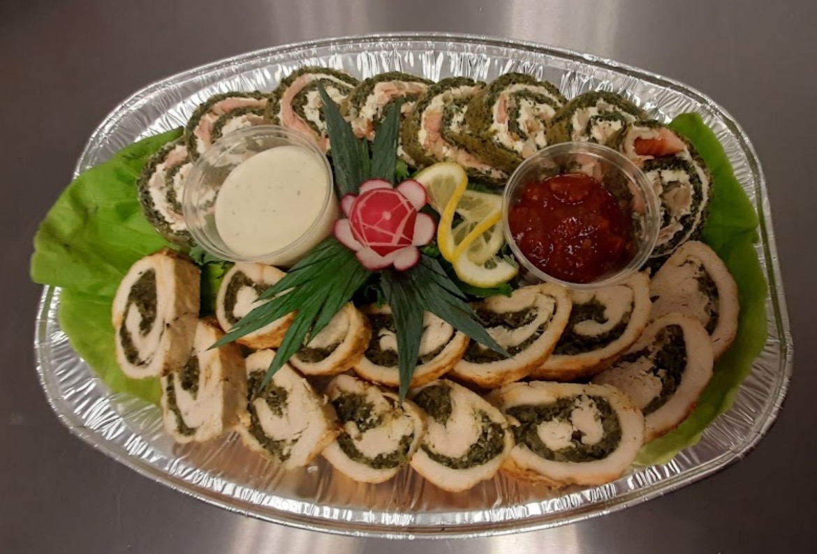 Dekoracyjna taca z roladkami mięsnymi i rybnymi ze szpinakiem, podana z sosem śmietanowym i sosem pomidorowym, ozdobiona rzodkiewką i cytryną.