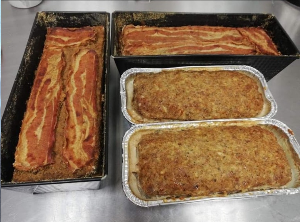 Cztery formy z pieczenią: dwie w aluminiowych foremkach, dwie w czarnych blaszanych, jedna z pieczeni w blaszanej formie przykryta plastrami boczku.