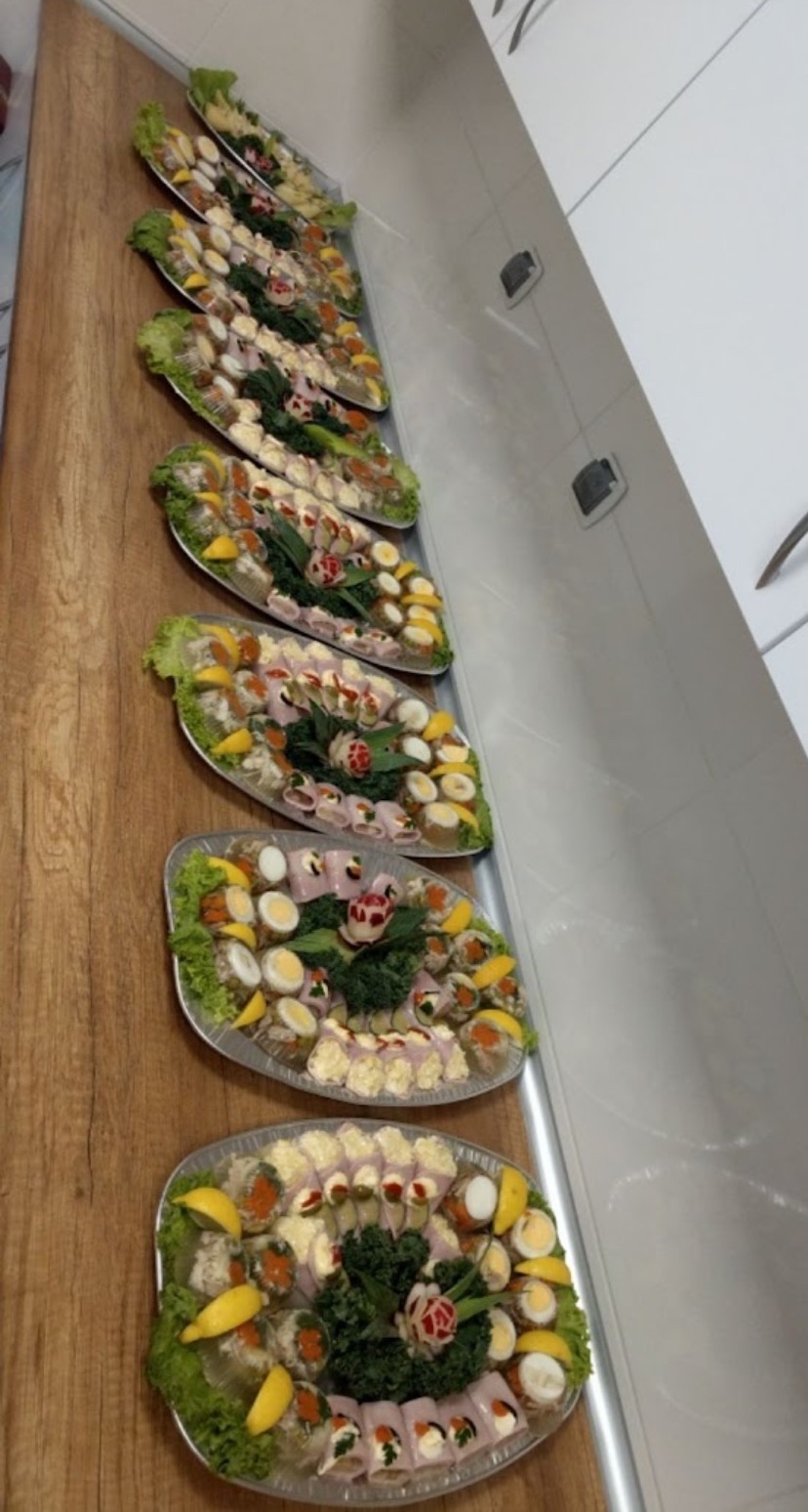 Rząd srebrnych pater z dekoracyjnymi przekąskami: roladki z szynki, jajka przepiórcze, koreczki, galaretki z kawiorem i cytryną, ozdobione sałatą i zielonymi warzywami, na drewnianym blacie przy...