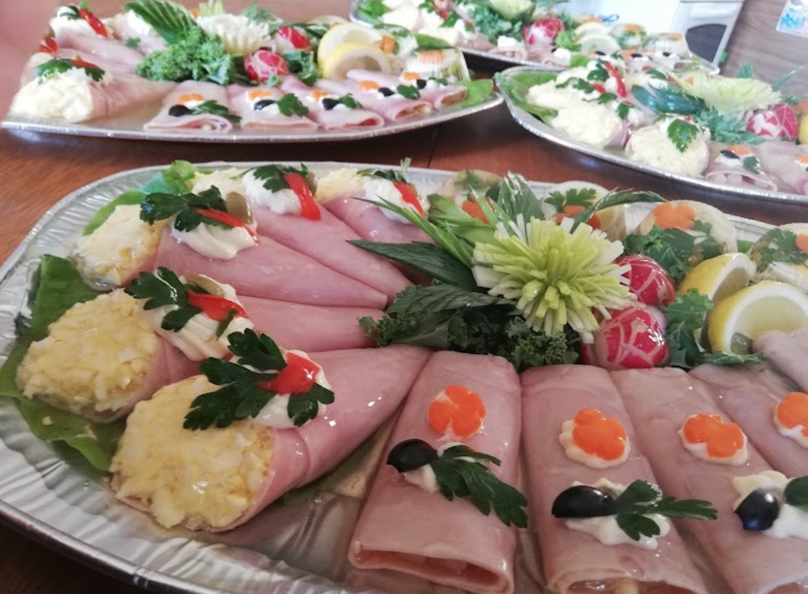 Dekoracyjne półmiski z roladkami z szynki, jajkami w majonezie i galaretkami warzywnymi, udekorowane świeżymi ziołami, na drewnianym stole.