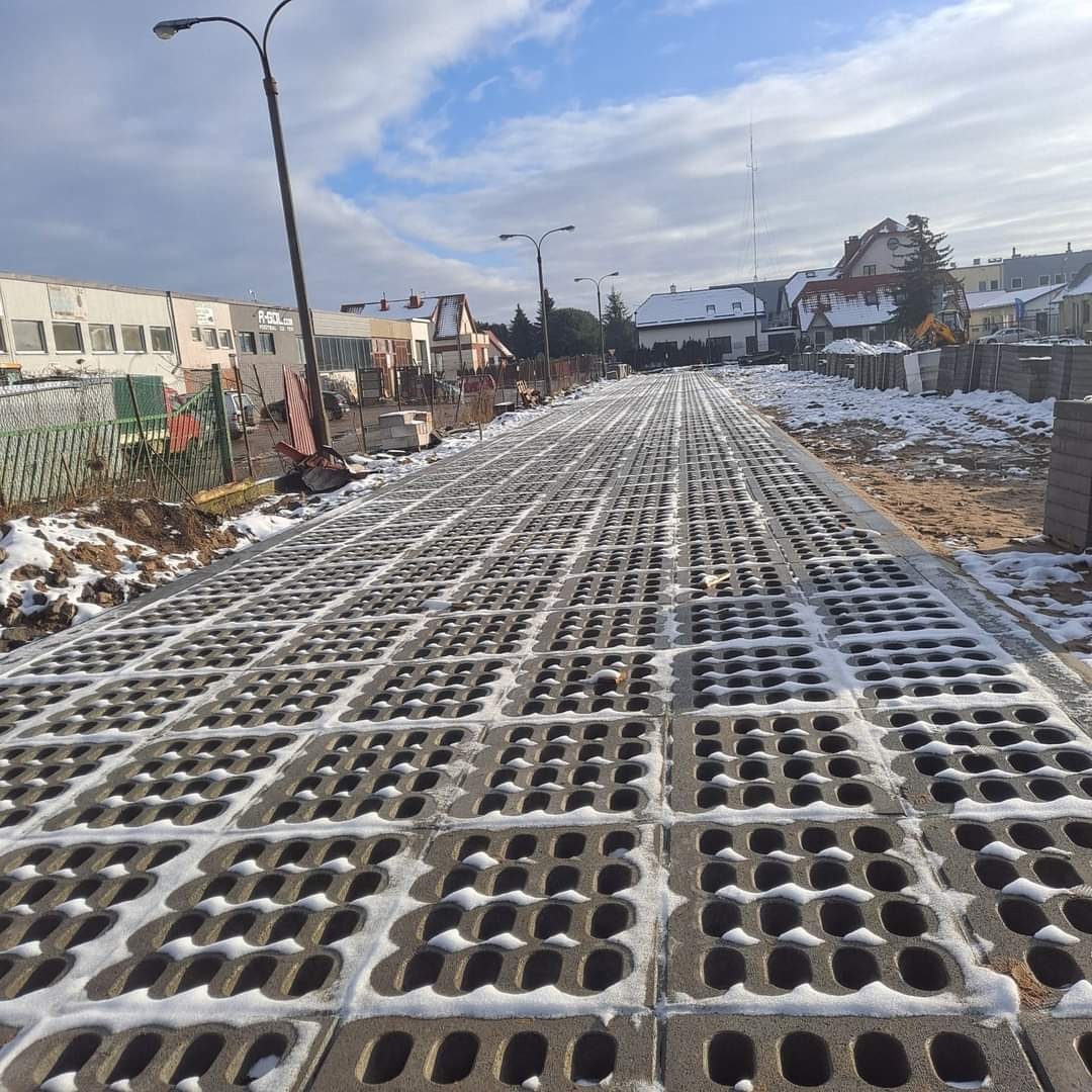 Układanie ażurowych płyt betonowych na parkingu w Dąbrównie, z resztkami śniegu w otworach, widok z perspektywy osoby stojącej na parkingu.